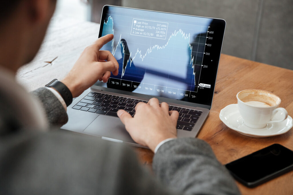Person using laptop to analyze market graph with coffee.