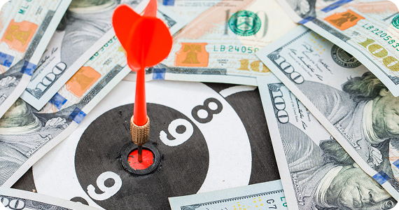 Red dart hits bullseye on target with $100 bills.