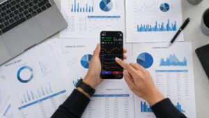 Business person reviewing financial data and graphs on a mobile device surrounded by reports