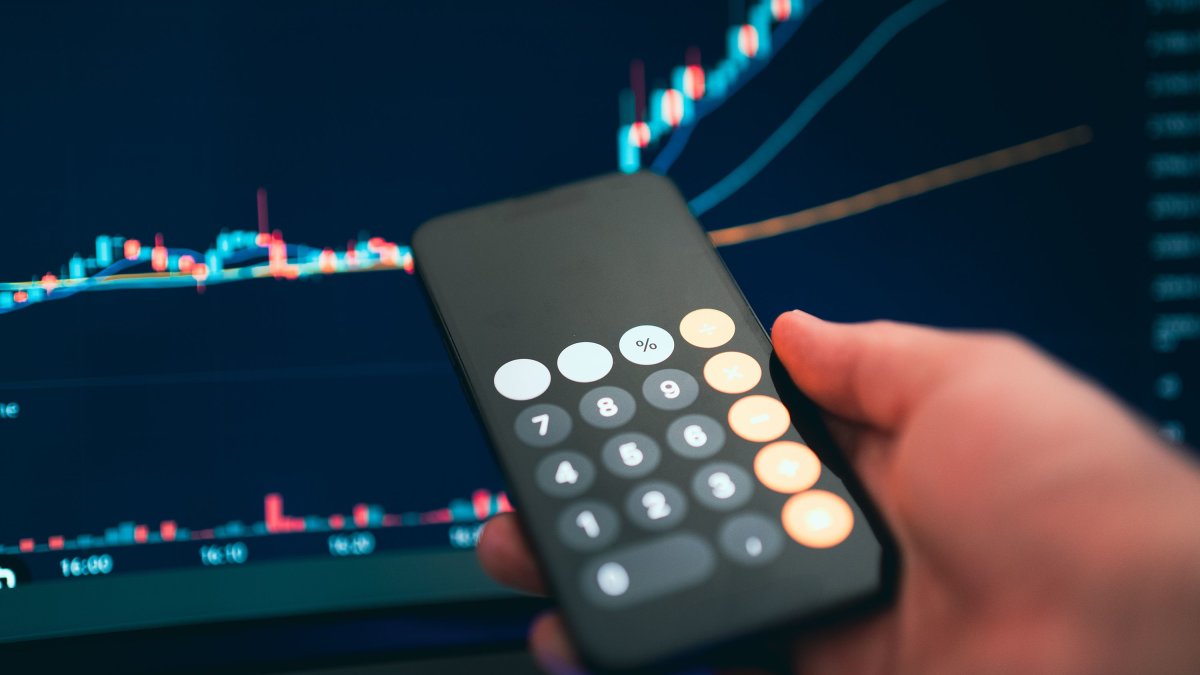 Close-up of a calculator on a smartphone with financial charts in the background
