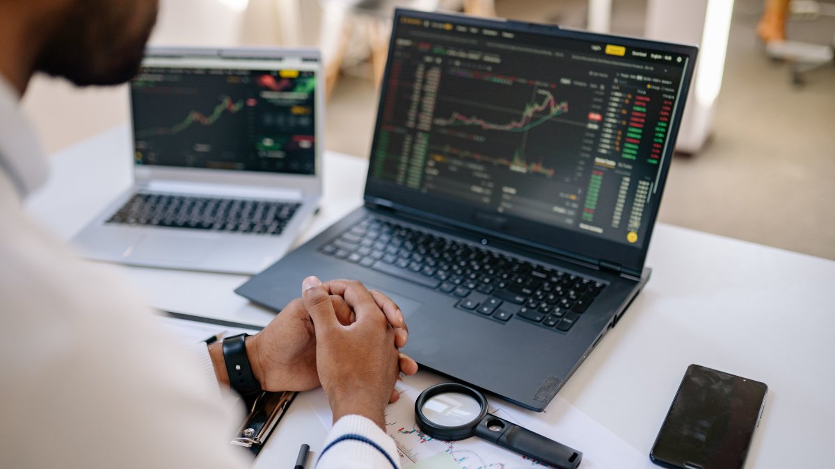 Business professional analyzing stock market data on dual laptops
